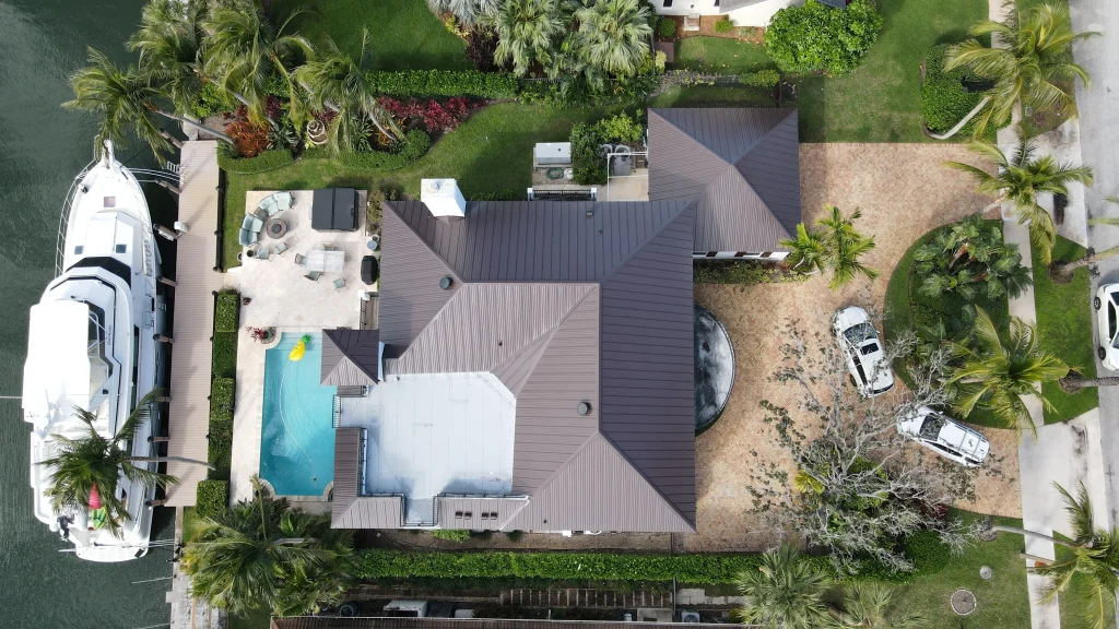 Bird's-eye view of a completed residential bronze metal roof installation on a tropical South Florida estate featuring a backyard swimming pool and a luxury yacht docked out back.