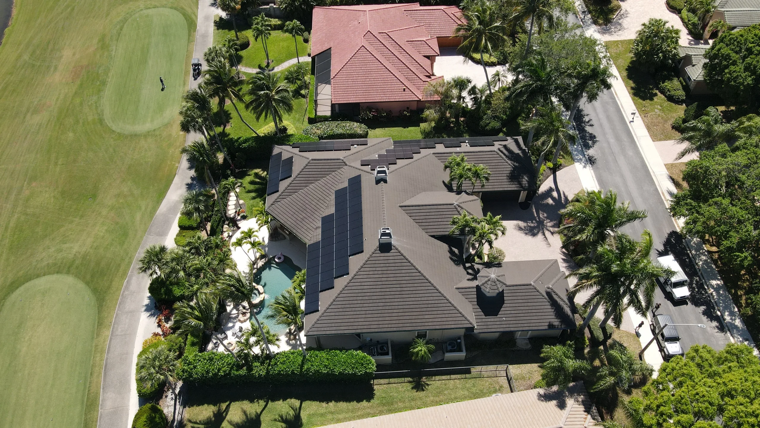 Overhead drone view of a luxury residential concrete tile roof with integrated solar panels, bordering a golf course green in Palm Beach Gardens, Florida, completed by Ace Pro Roofing.
